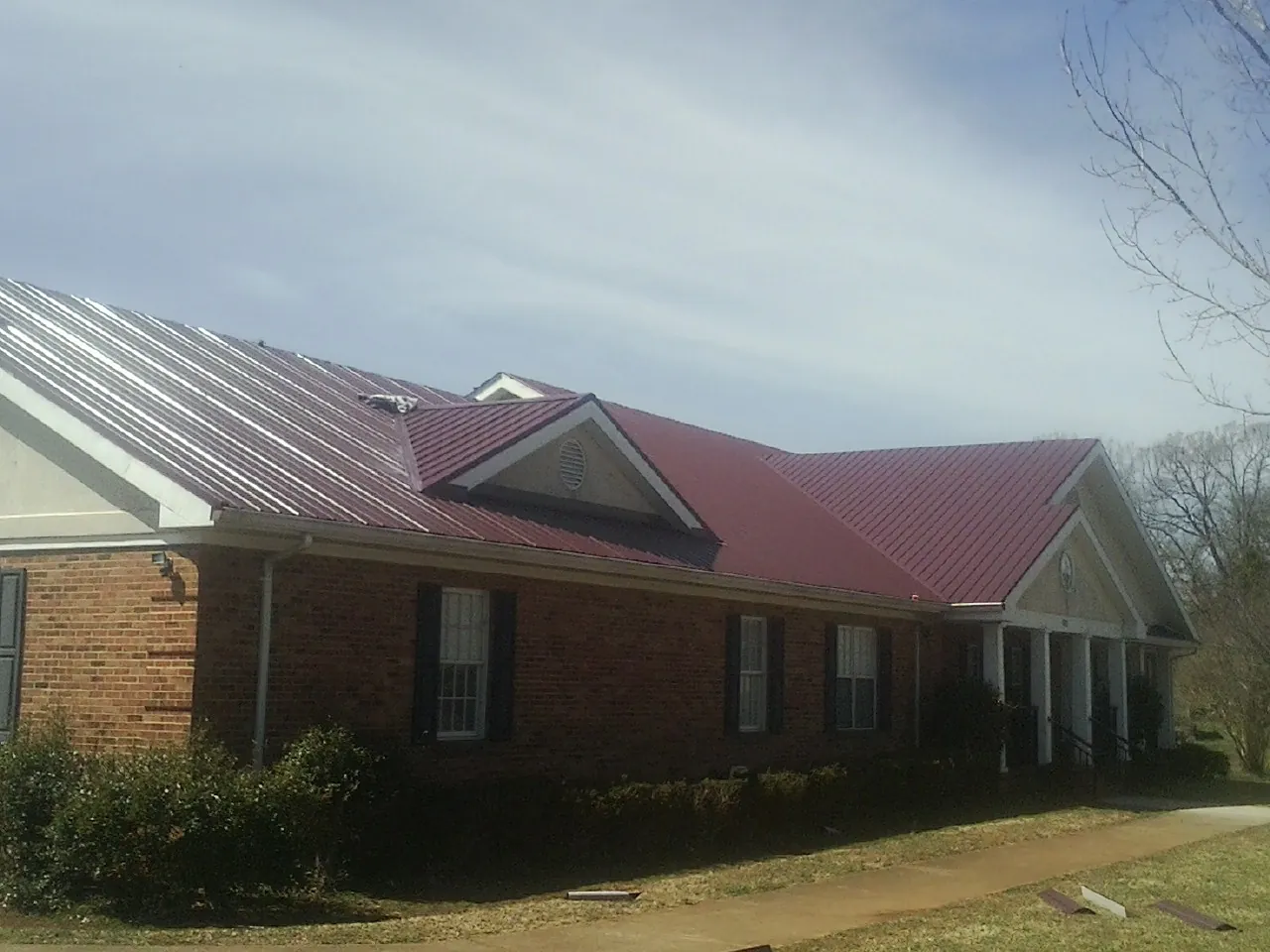 Red metal roof with gabled entries on a long brick building, from a Hail Damage Roof Repair job in Josephine