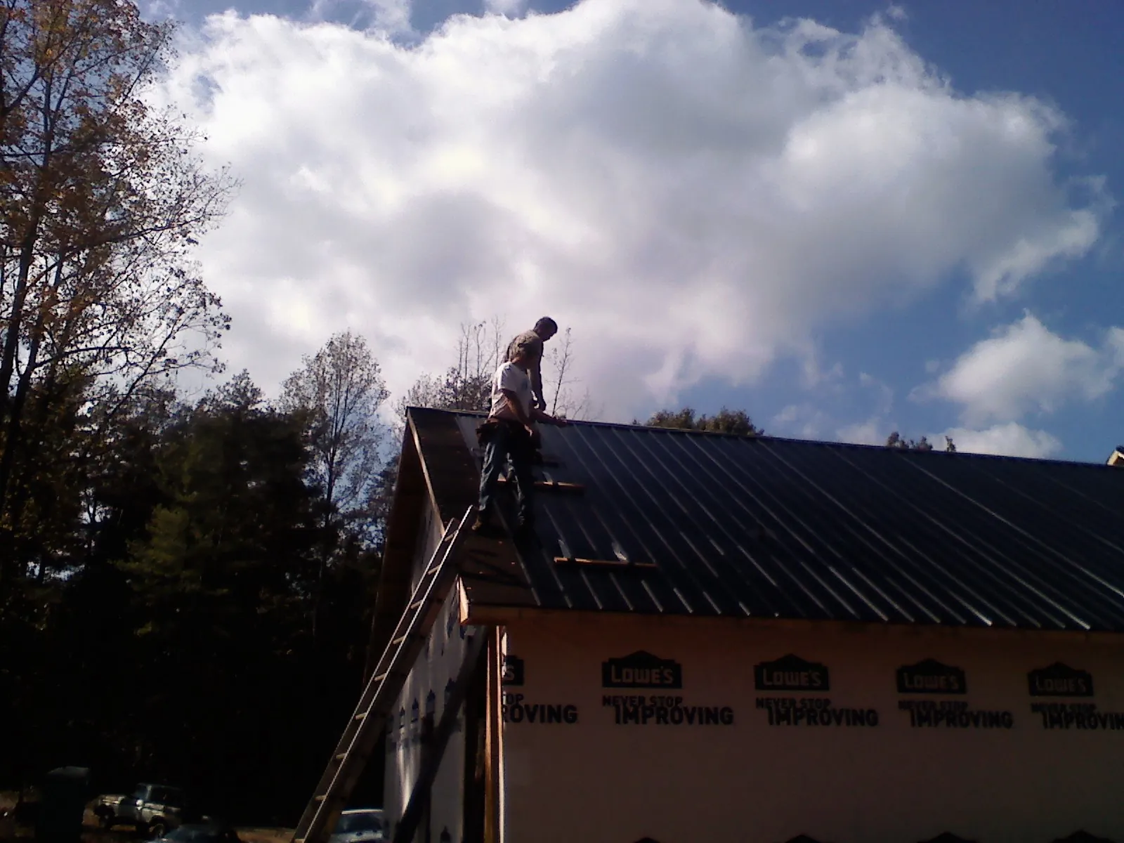 Roofer fastening dark metal panels high against a cloudy sky, from a Roof Inspection job in Josephine