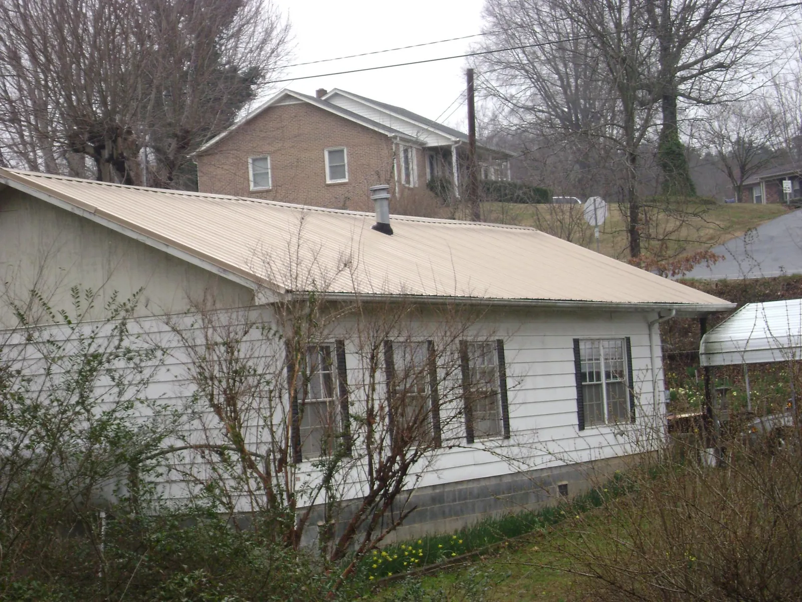 Tan metal roof on a white sided house set into a hillside — Commercial Roofing by Roofing Brothers in Josephine